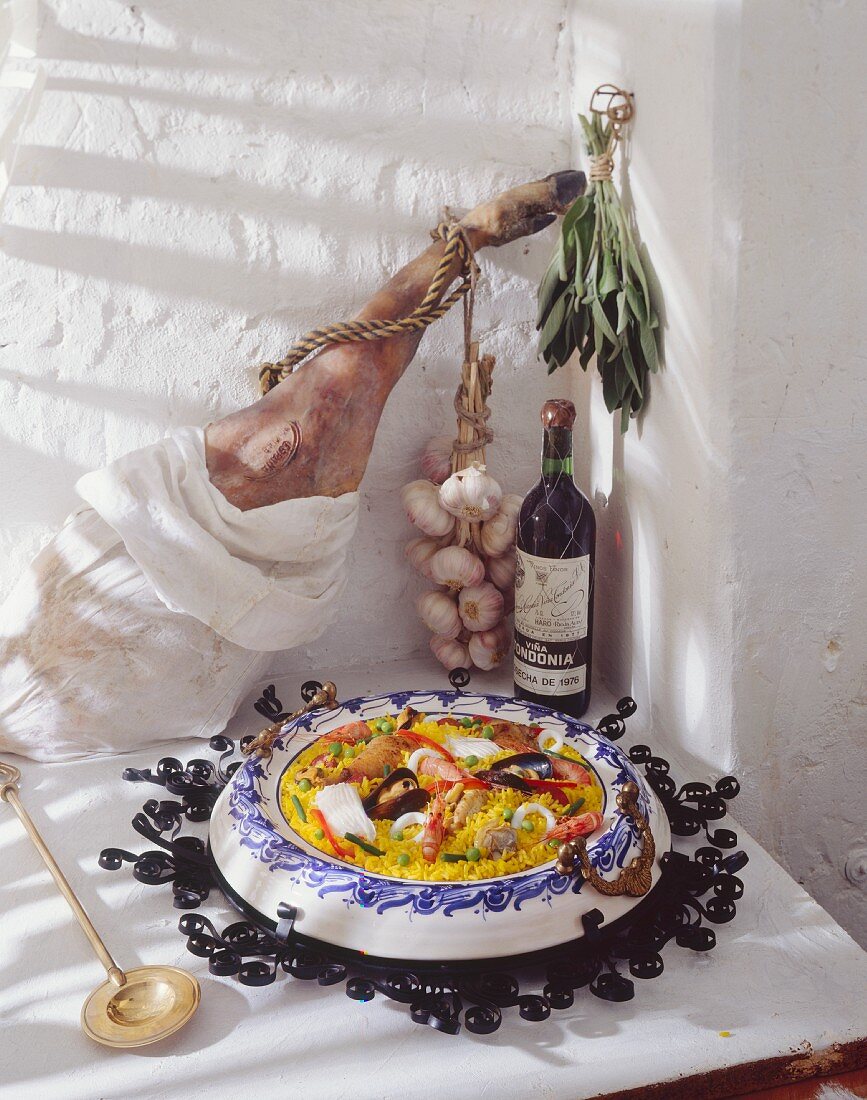 Eine Paella, dahinter Lammkeule, Rotwein, Knoblauch