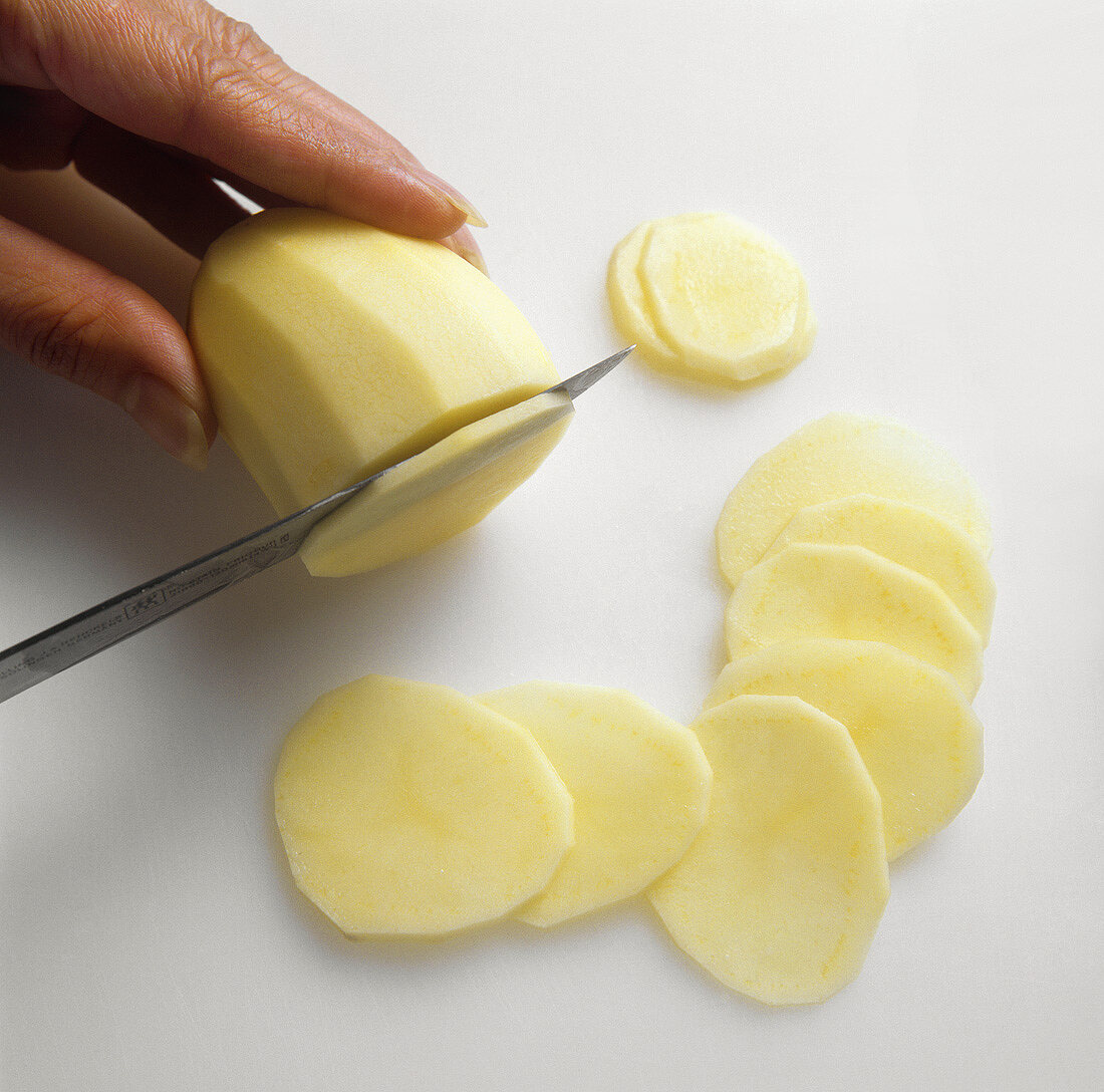 Eine geschälte Kartoffel in Scheiben schneiden