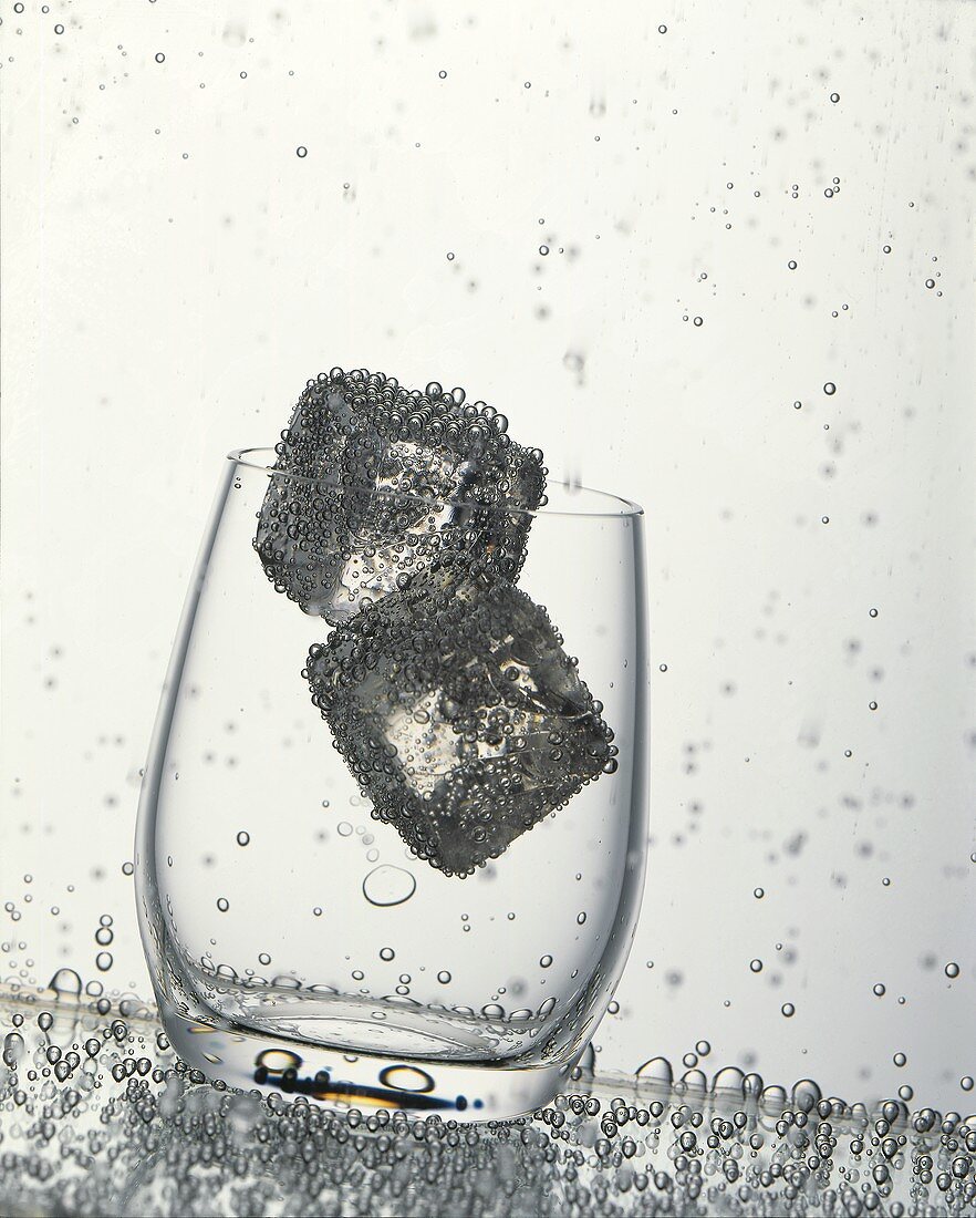 Glas mit Eiswürfeln in sprudelndem Wasser