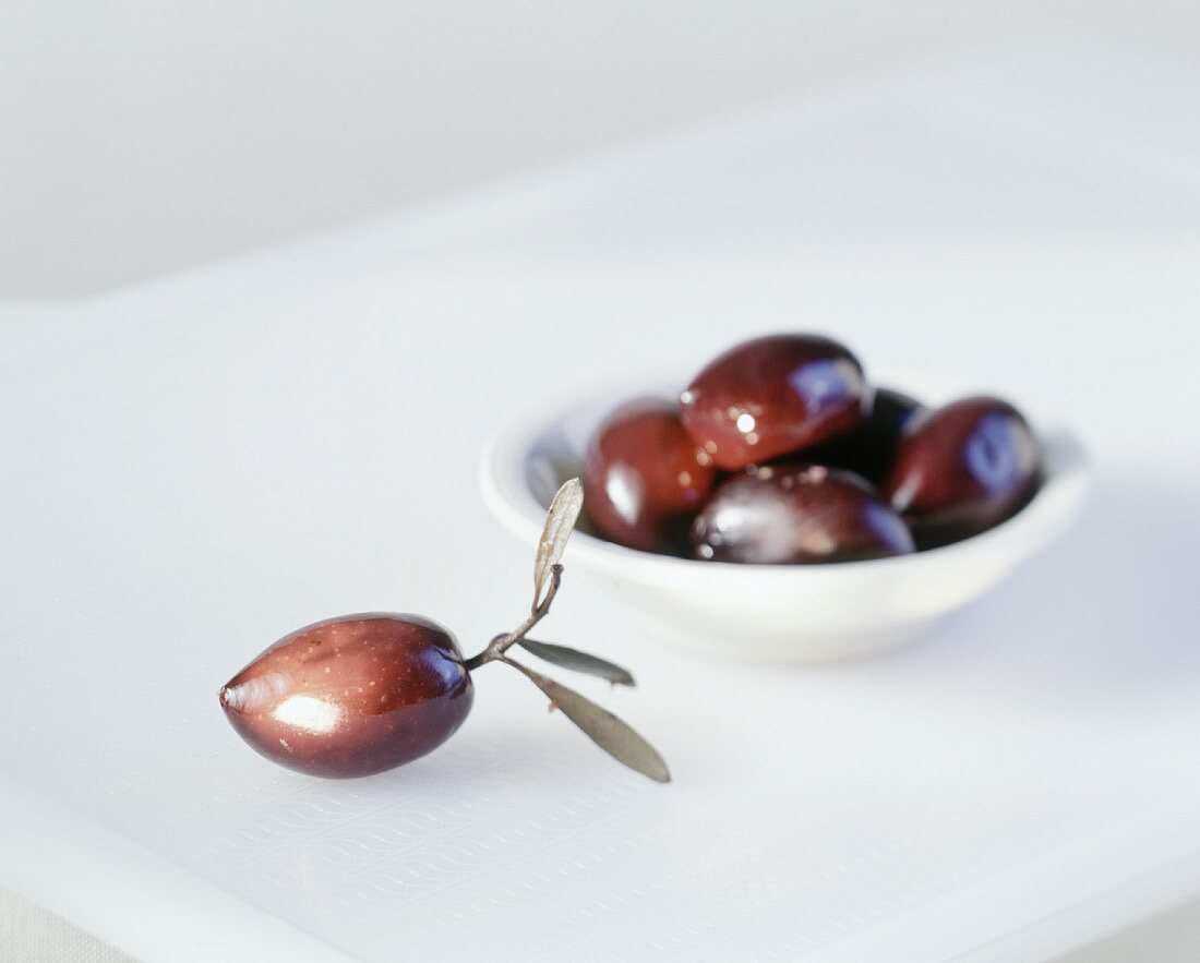 Eine Olive mit Blättern daneben ein Schälchen mit Oliven