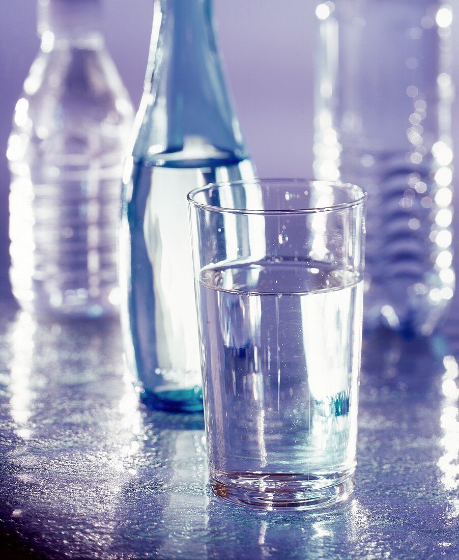 Ein Glas Mineralwasser mit Wasserflaschen im Hintergrund