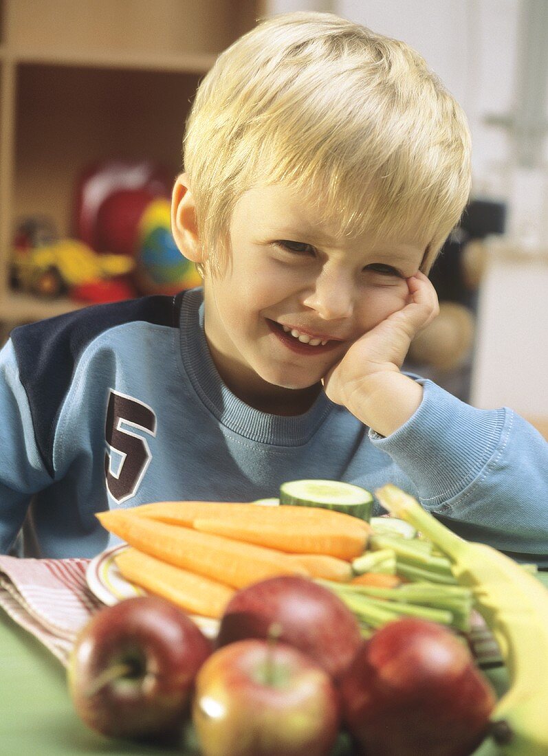 Kleiner Junge sitzt am Tisch mit Obst und Gemüse