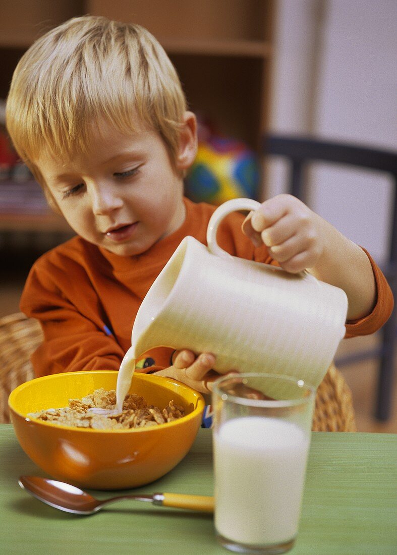 Kleiner Junge giesst Milch über Cornflakes