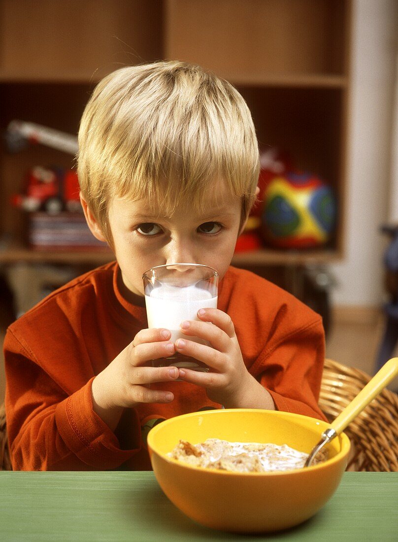 Kleiner Junge trinkt Milch, vor ihm Cornflakes