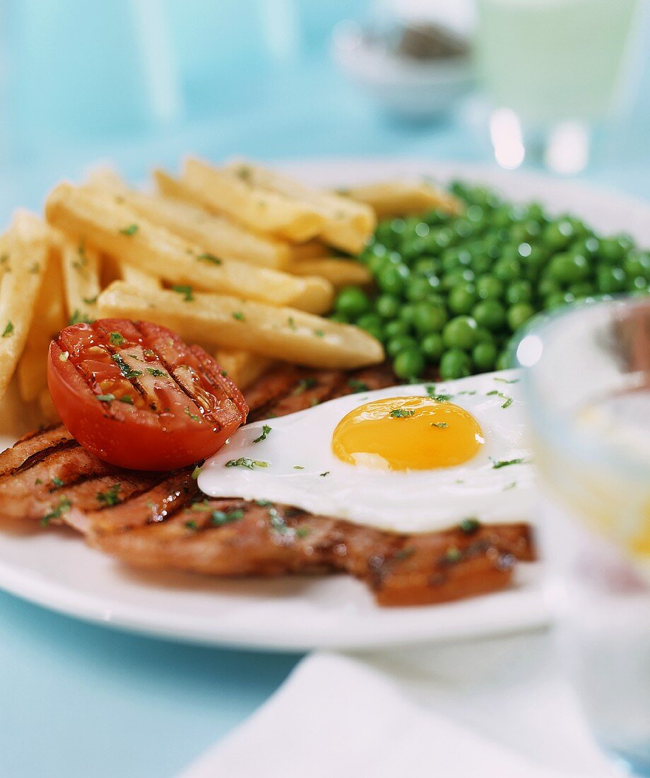 Fried egg with fried ham, peas and chips