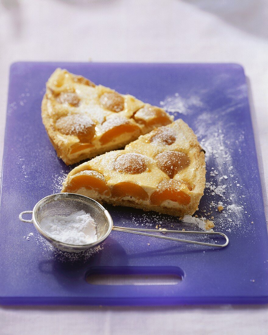 Quark tart with apricots, sieve with icing sugar in front