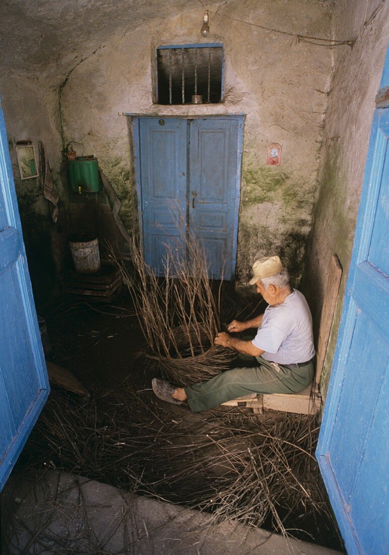 Alter Mann flechtet Korb aus dünnen Ästen, Santorini