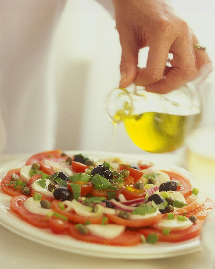 Mozzarella auf Tomaten (Caprese) mit Olivenöl beträufeln