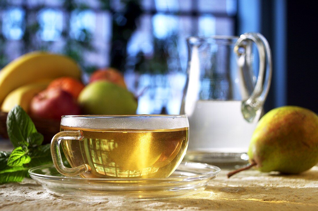 Eine Tasse Tee, Früchte und ein Krug Wasser