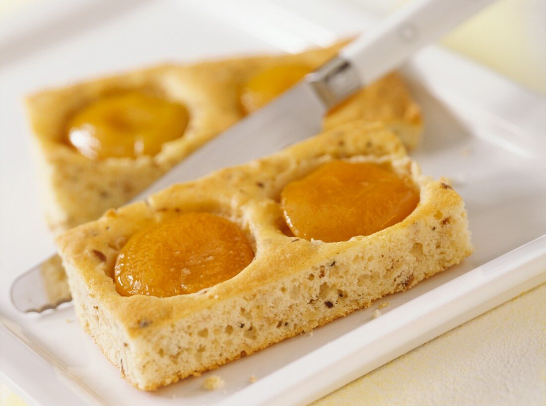 Tray-baked peach cake being cut into pieces