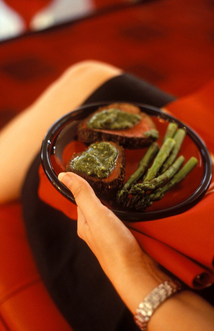 Woman holding plate of roast beef with pesto & asparagus