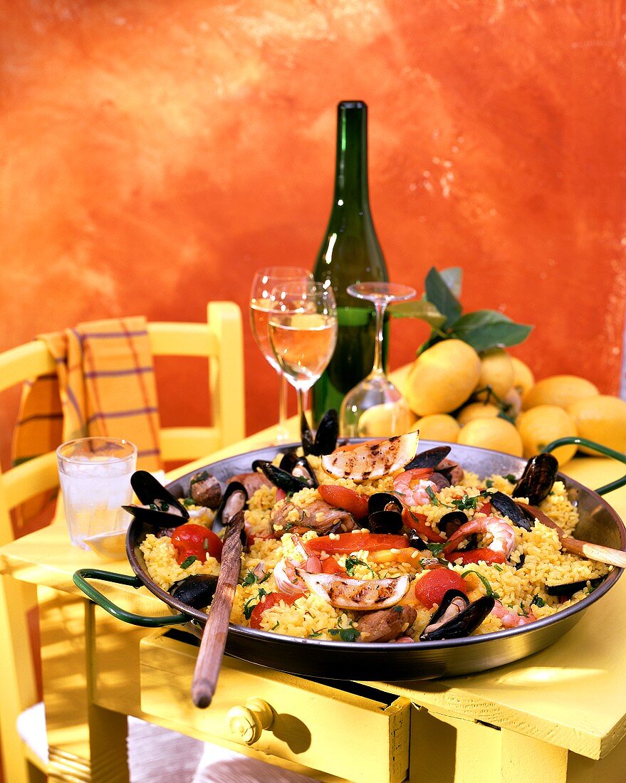 Paella in einer klassischen Paellapfanne auf gelbem Tisch