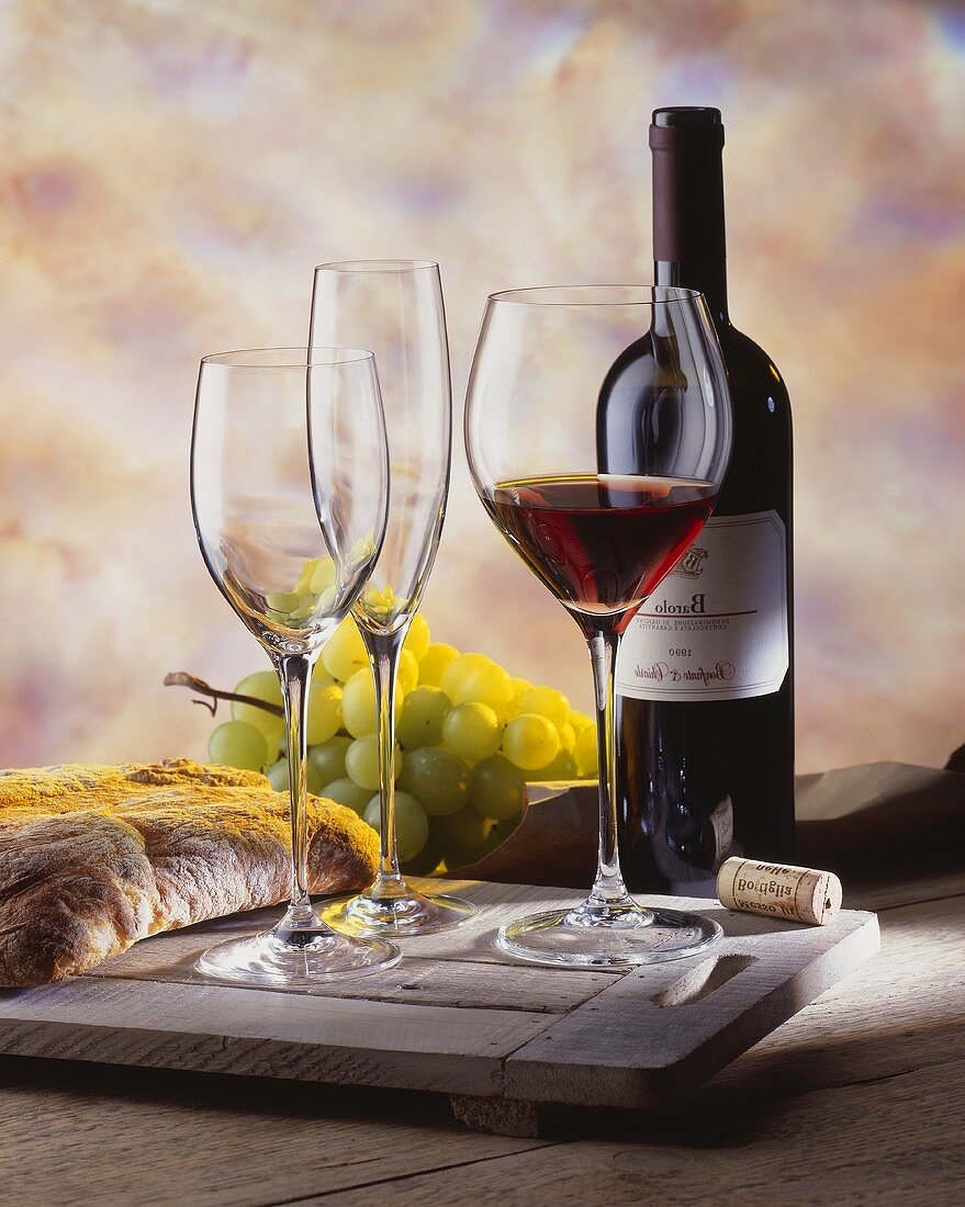 Rotweinstilleben mit Barolo, Gläsern, Trauben und Brot