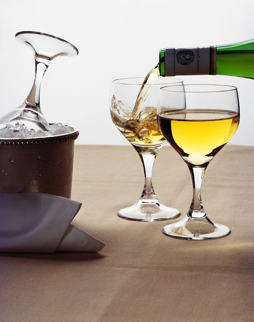 Weißwein einschenken, daneben Kühler und gefülltes Glas