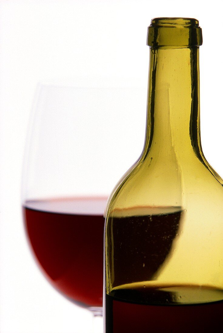 Red wine bottle with glass in background (close-up)