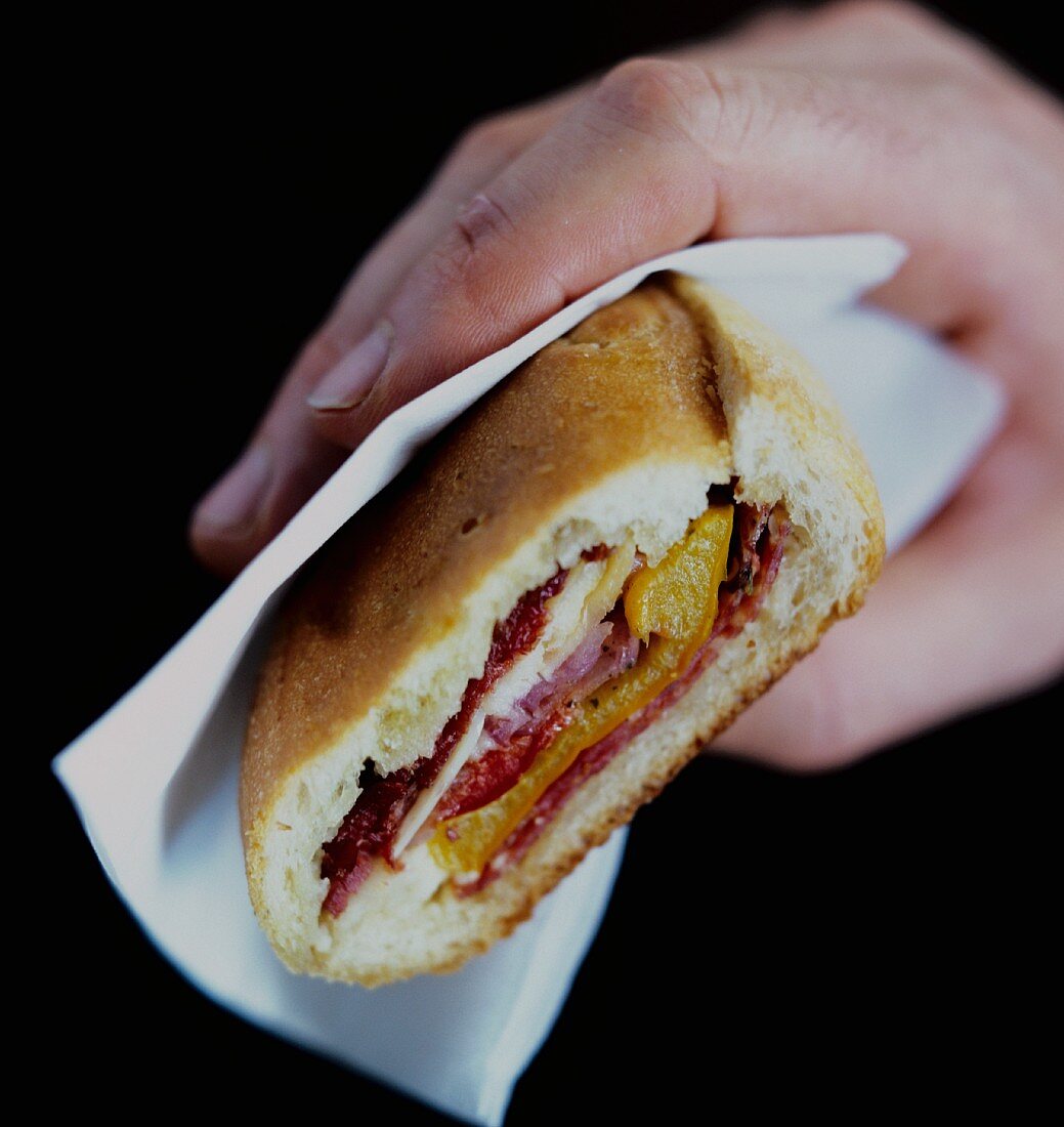Hand holding panini with pepper, salami and cheese