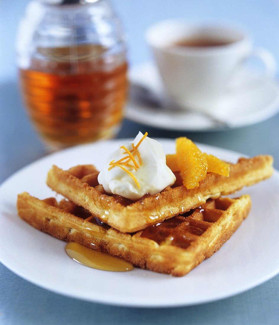 Orange waffles with cream and maple syrup and a cup of tea