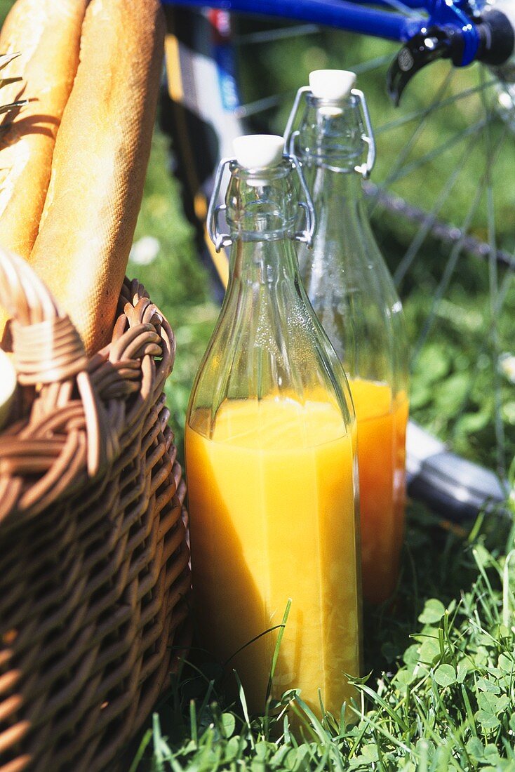 Orange and carrot juice in bottles beside picnic basket
