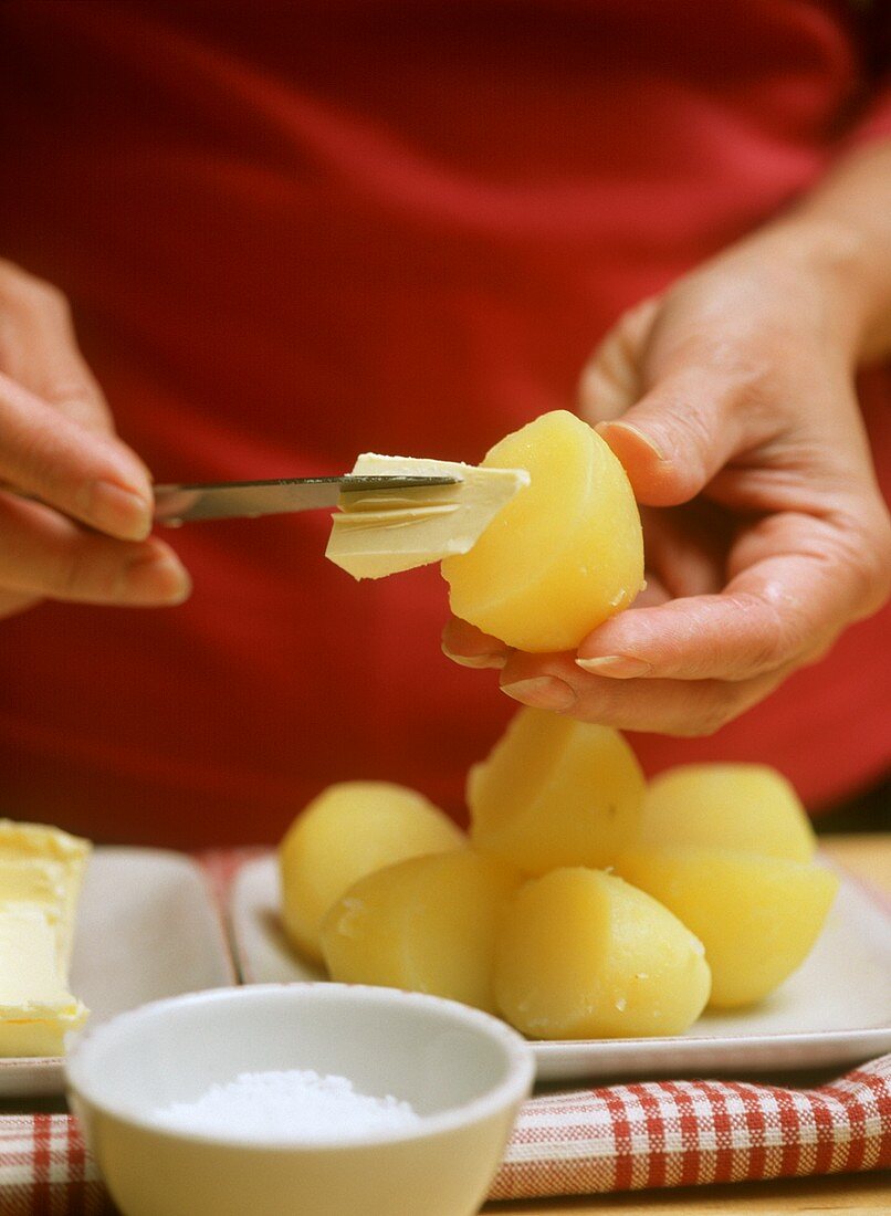 Person streicht Butter auf Pellkartoffel,davor Schälchen Salz