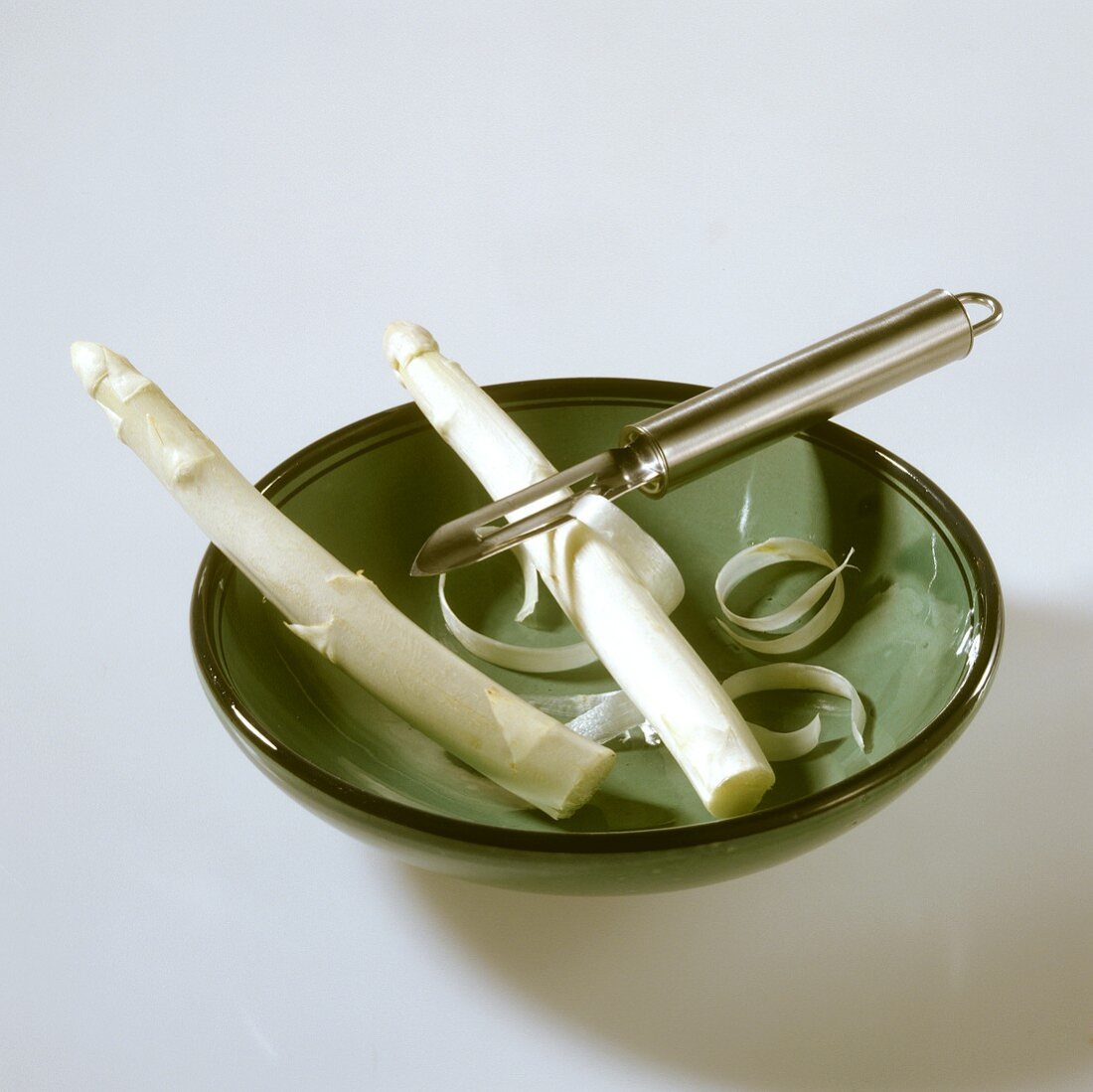 Two spears of white asparagus with vegetable peeler