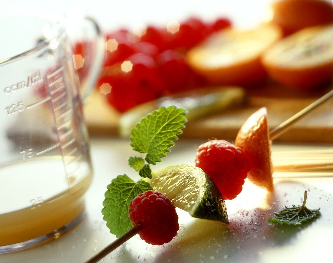 Still life with fruit kebab, juice in measuring jug & fruit