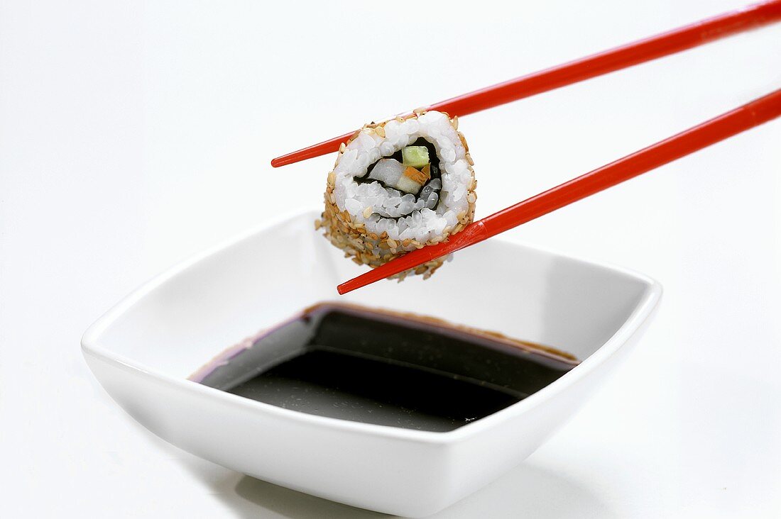 Stäbchen mit Ura-Maki-Sushi (Inside-Out-Roll) über Sojasauce