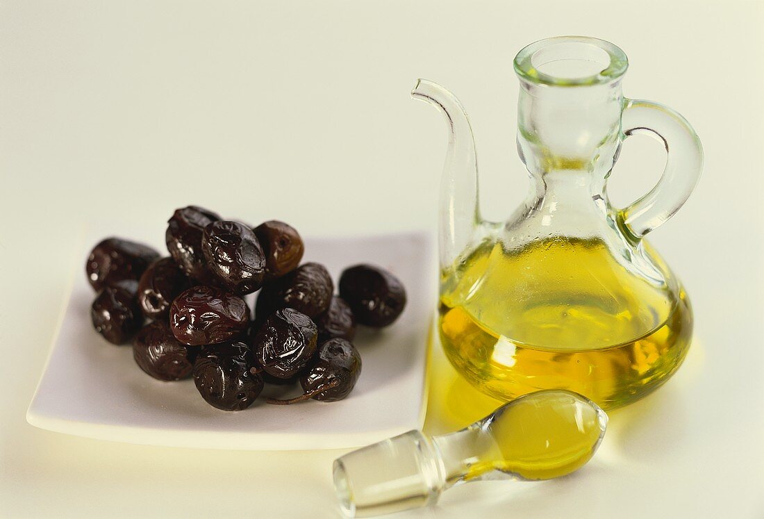 Kleine Karaffe mit Olivenöl und Oliven auf einem Teller