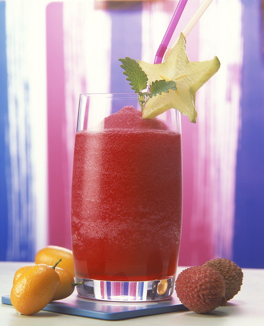 Frozen strawberry drink in glass, fresh fruit beside it
