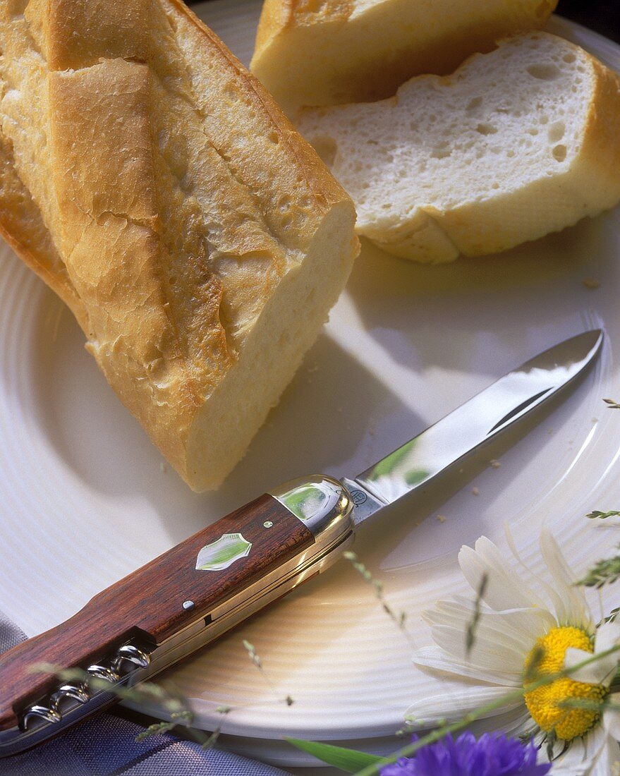 Baguette in the piece and sliced with jack-knife on plate