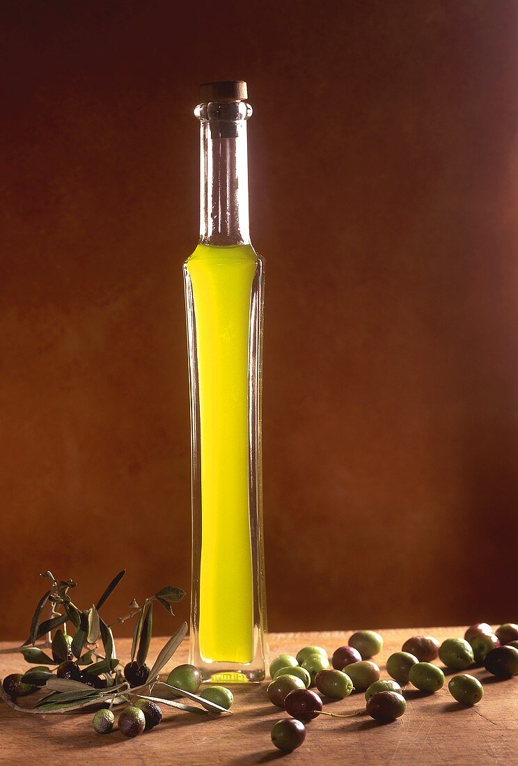 Olivenöl in einer langen, schlanken Glasflasche mit Oliven