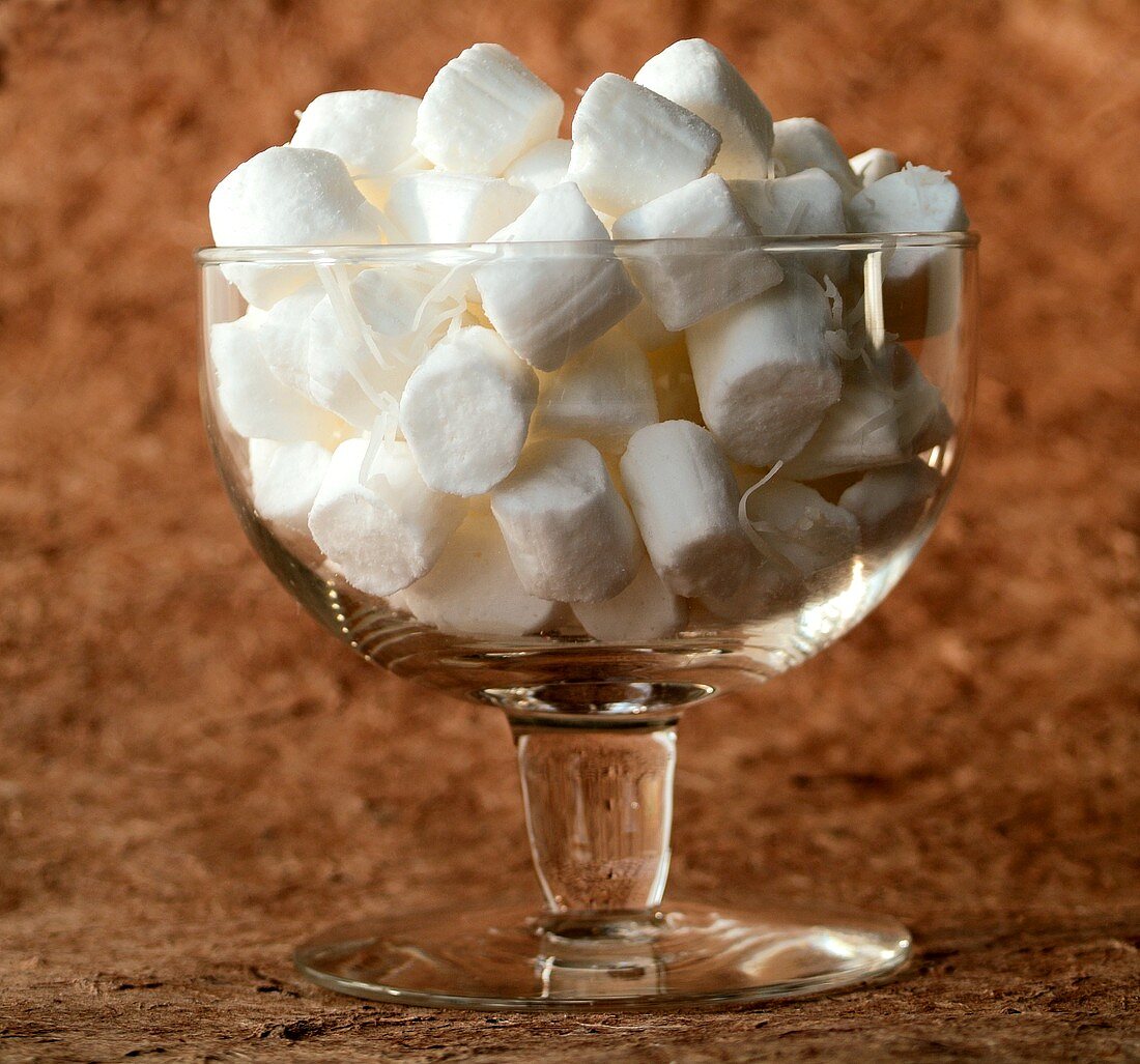 Glass bowl with coconut sweets against brown background