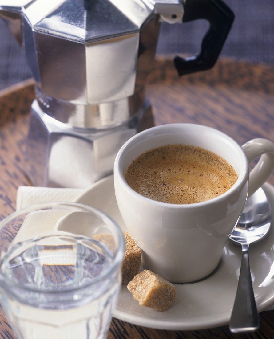 Tasse Espresso mit Wasserglas und Maschine im Hintergrund