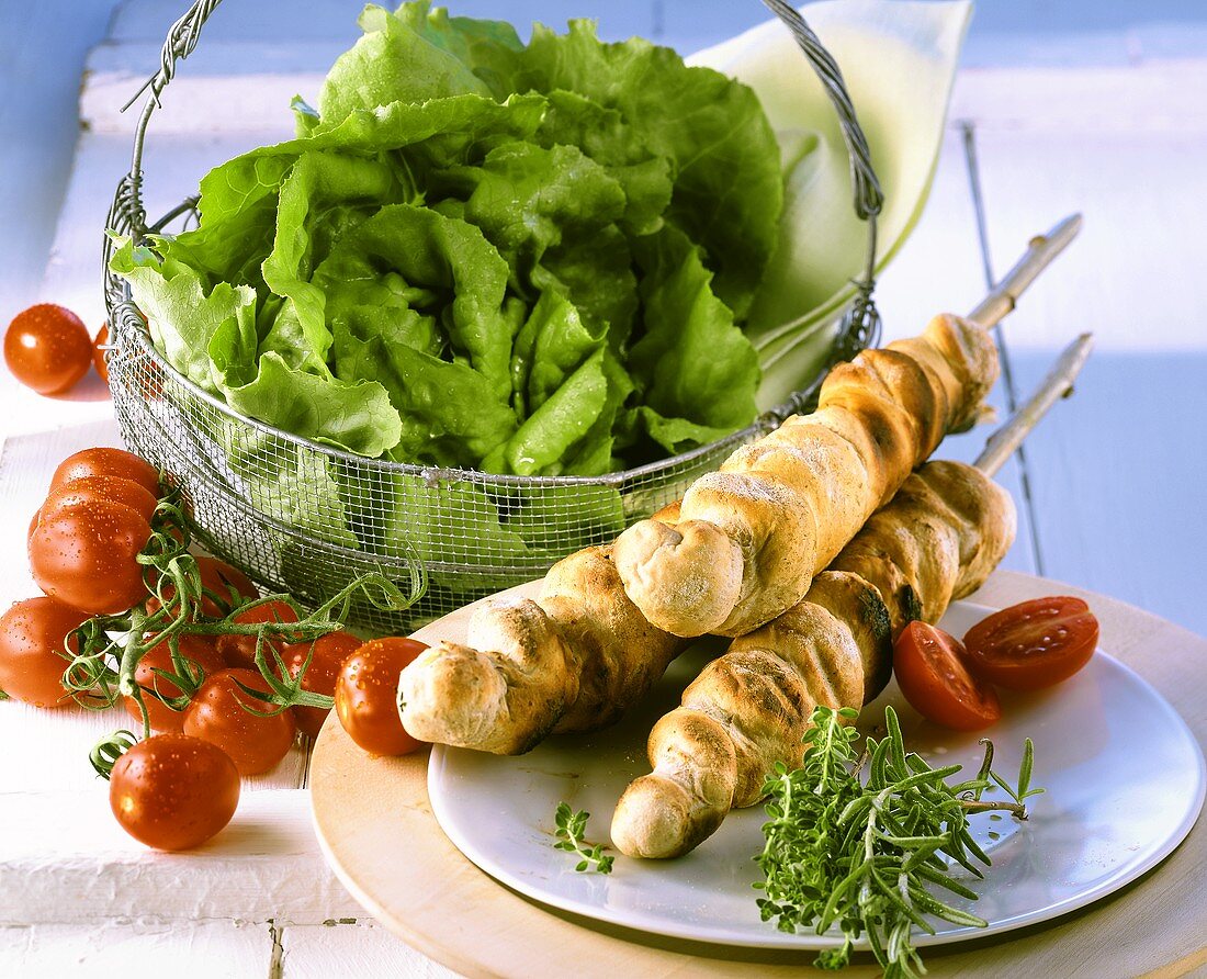 Barbecued bread sticks, basket of lettuce, tomatoes behind