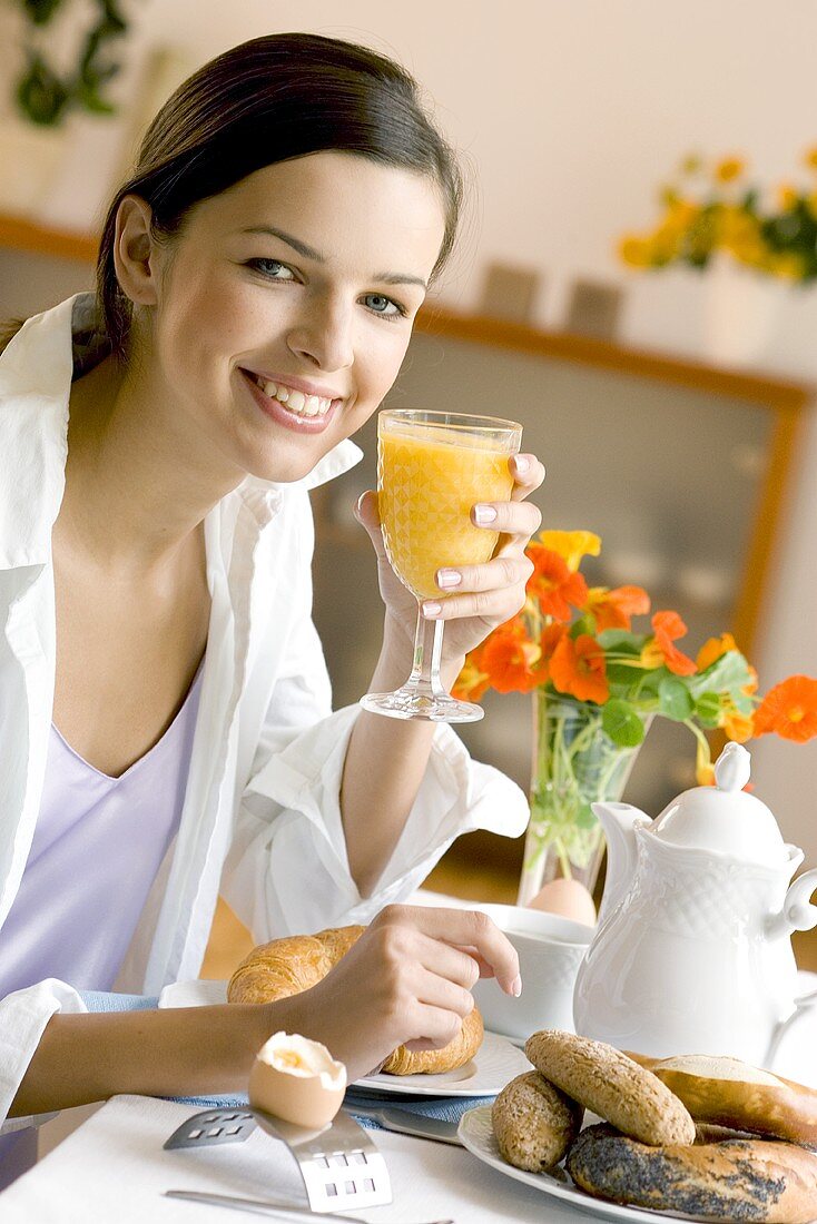 Junge Frau mit Orangensaft am Frühstückstisch