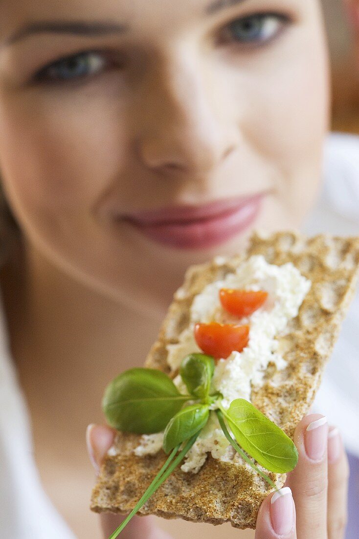 Young woman eating crispbread with herb quark (close-up)