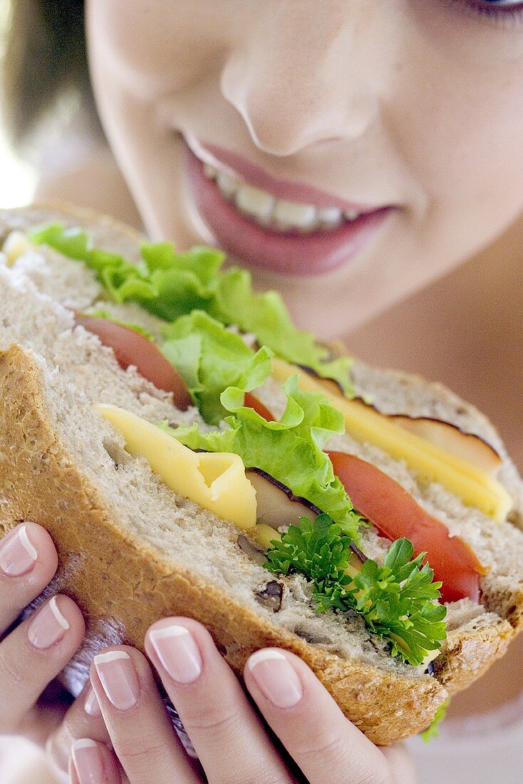 Young woman eating giant sandwich (close-up)