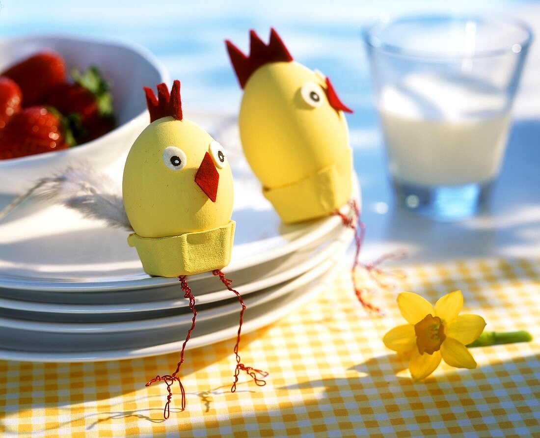 Zwei Ostereier als Hühnchen, auf einem Stapel Teller sitzend