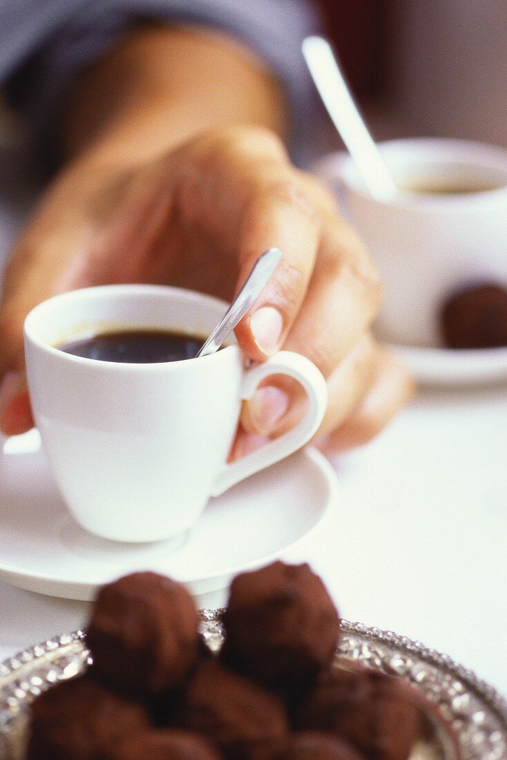 Hand holding a cup of espresso, rum truffles in front