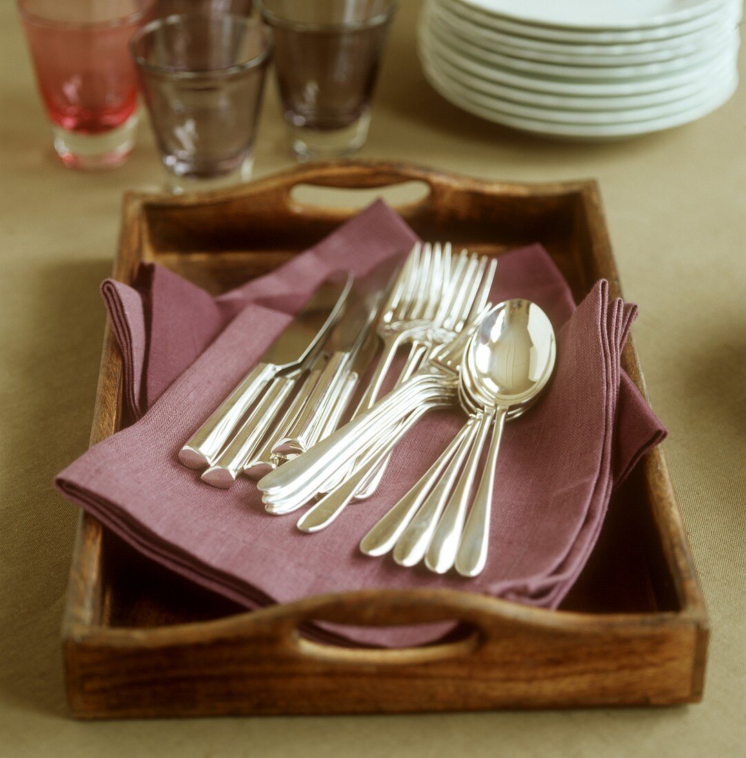 Cutlery on a tray, glasses and pile of plates behind