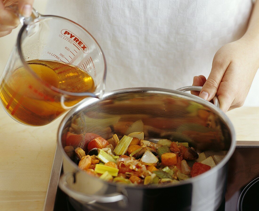 Pouring stock over vegetables for vegetable stew