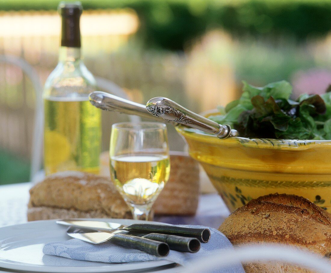 Gedeckter Tisch im Freien mit Salat, Brot und Wein