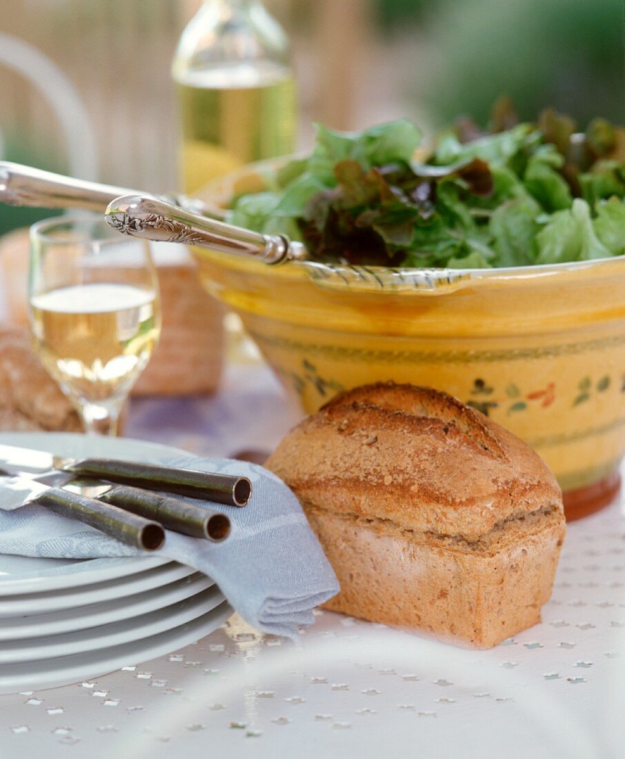 Gedeckter Tisch im Freien mit Salatschüssel, Brot & Geschirr