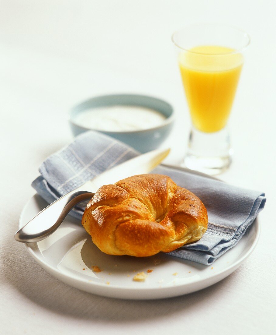 Croissant auf einem Teller, dahinter Glas mit Orangensaft