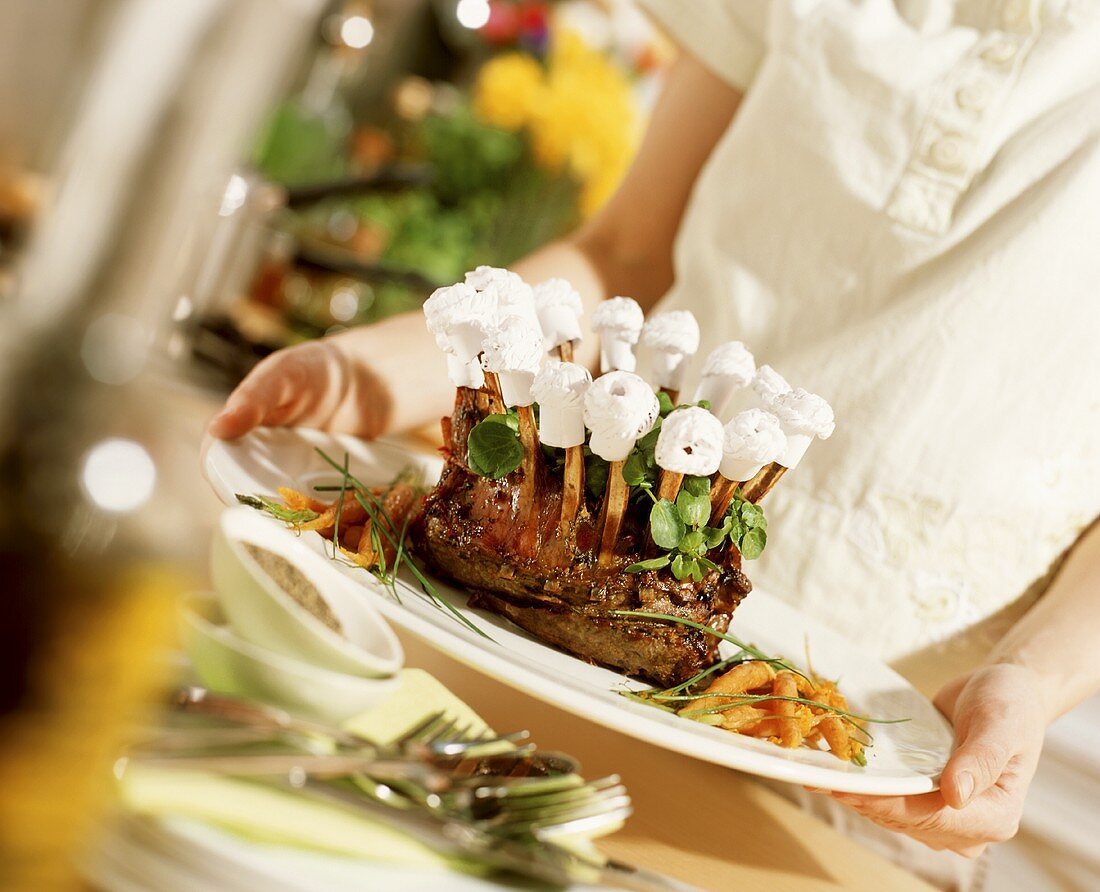 Woman putting a serving dish with rack of lamb on the table