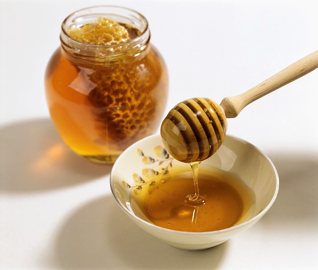 Honey dipper with fresh honey; jar with honeycomb