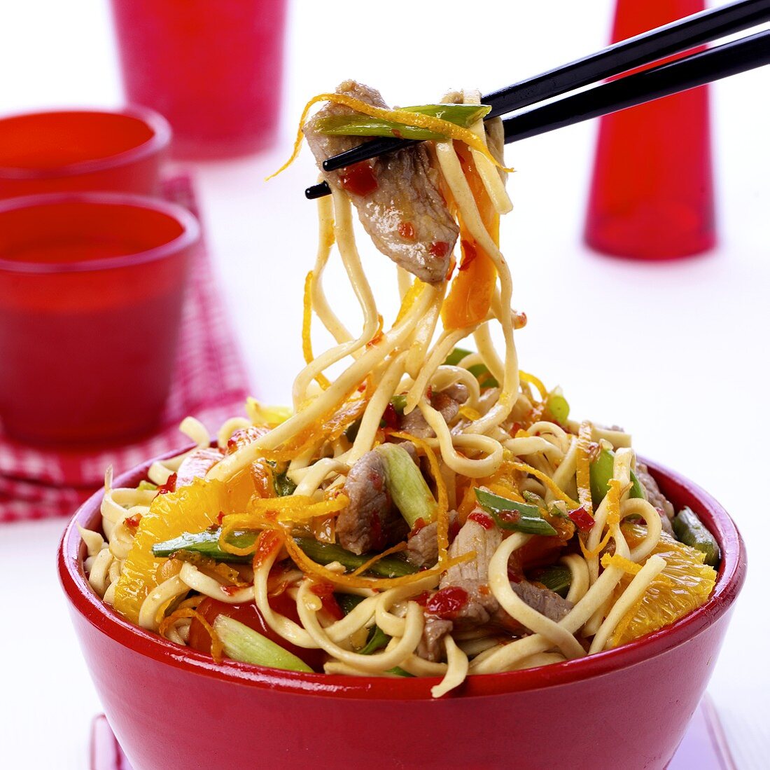 Chopsticks holding Asian stir-fry with meat, vegetables, oranges