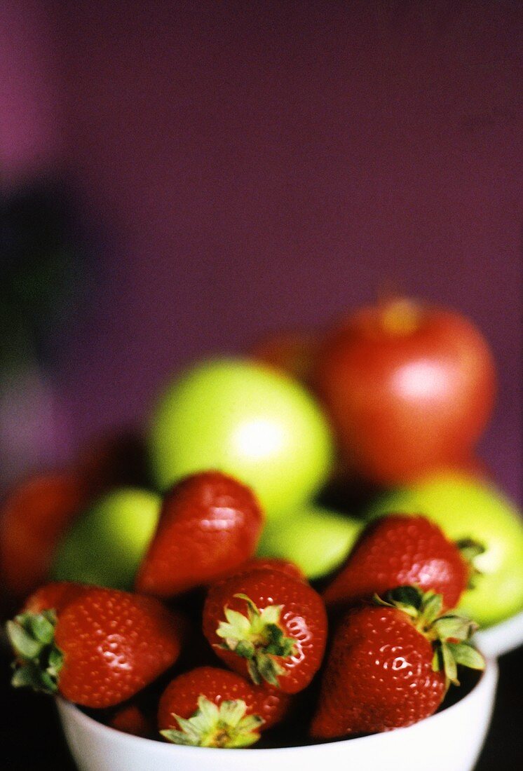 Bowl of strawberries, apples behind