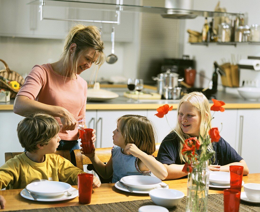 Mother pouring drinks for children sitting at table