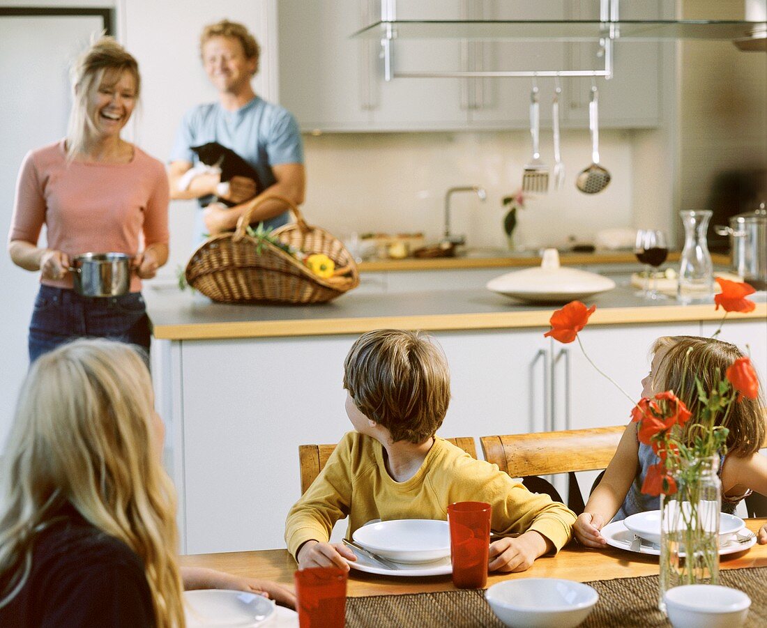 Kinder am Esstisch in der Küche, Mutter bringt den Kochtopf