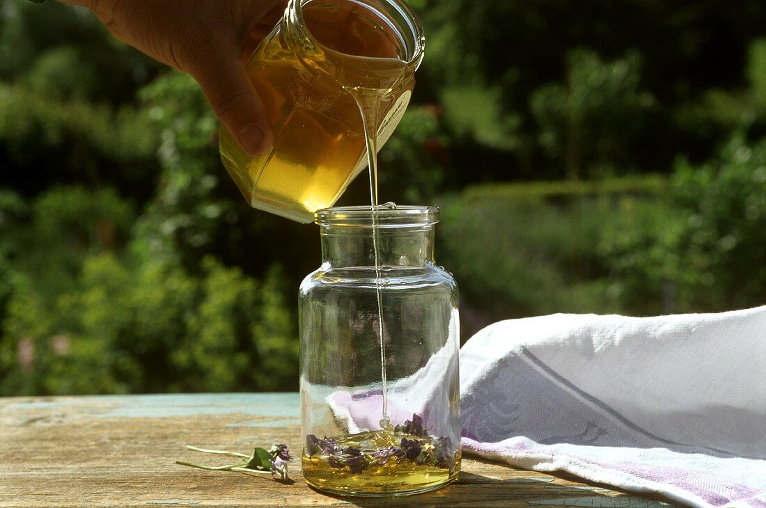 Pouring acacia honey over fresh edible flowers in jar 